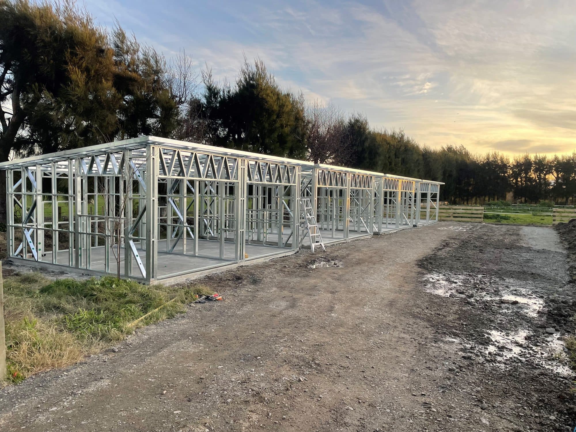Row of light gauge steel garage frames on concrete slabs at a rural site