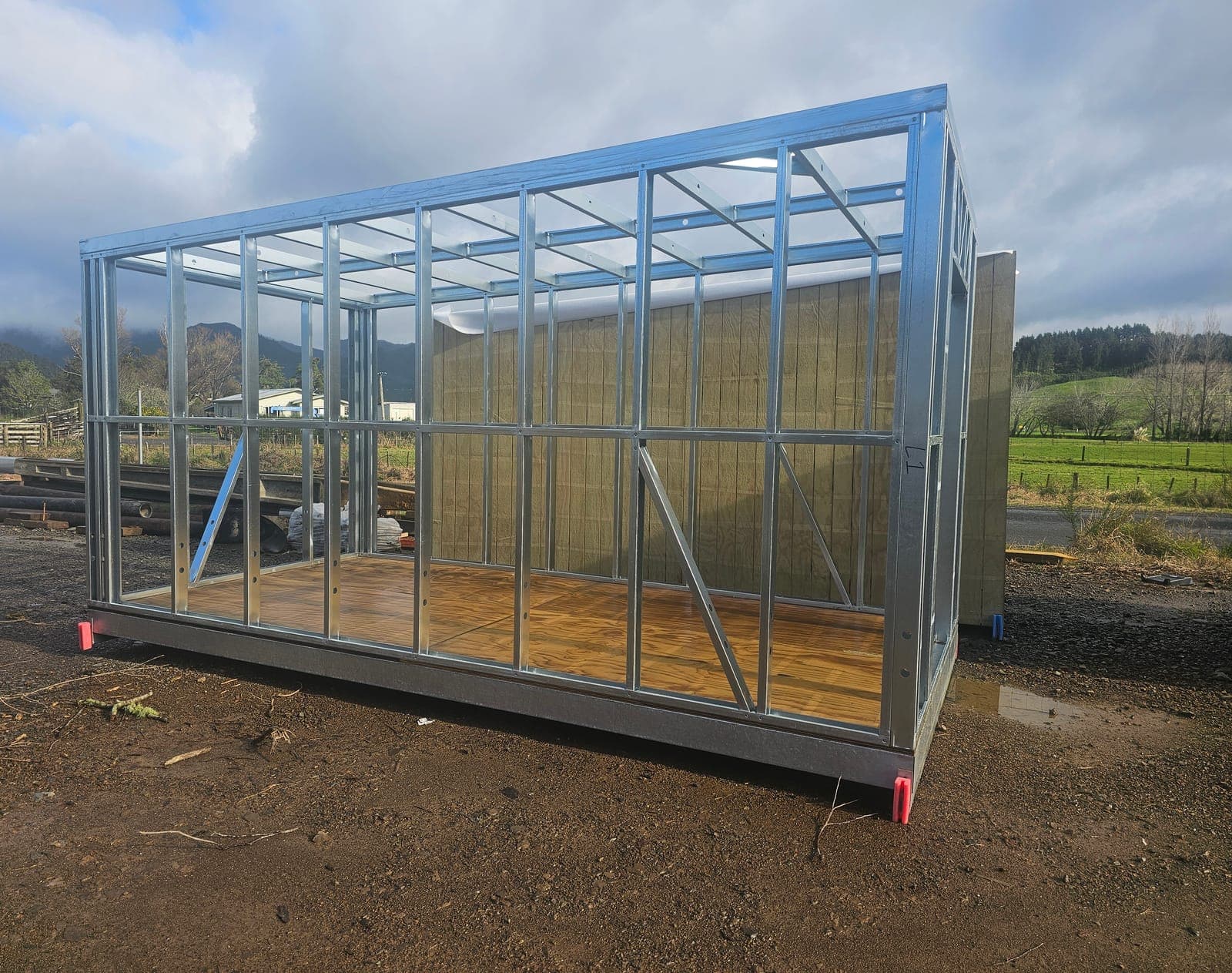 Galvanised steel wall frame standing on a timber floor panel at a rural site
